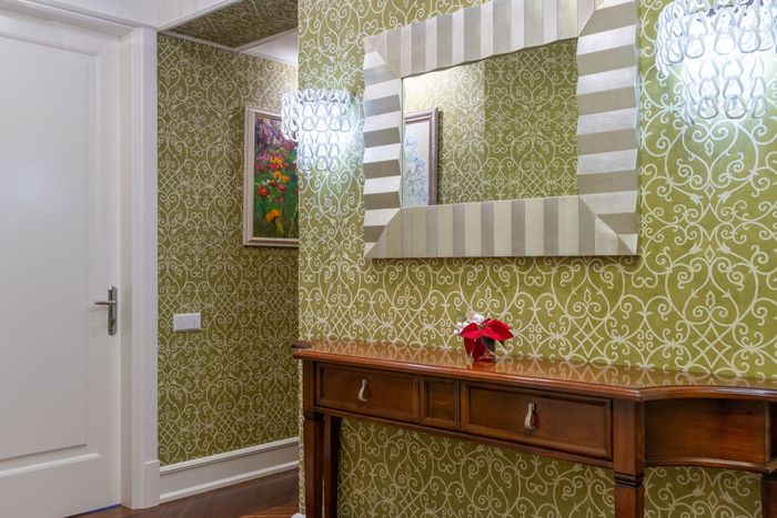 Hallway with green floral wallpaper, a wooden console table and a decorative mirror