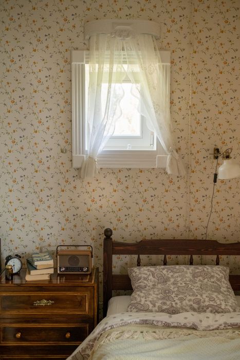Bedroom wall covered in delicate cream floral-sprig wallpaper beside a window