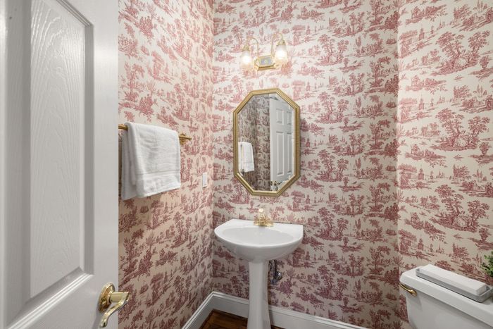 Powder room with red toile wallpaper, a pedestal sink and a framed mirror