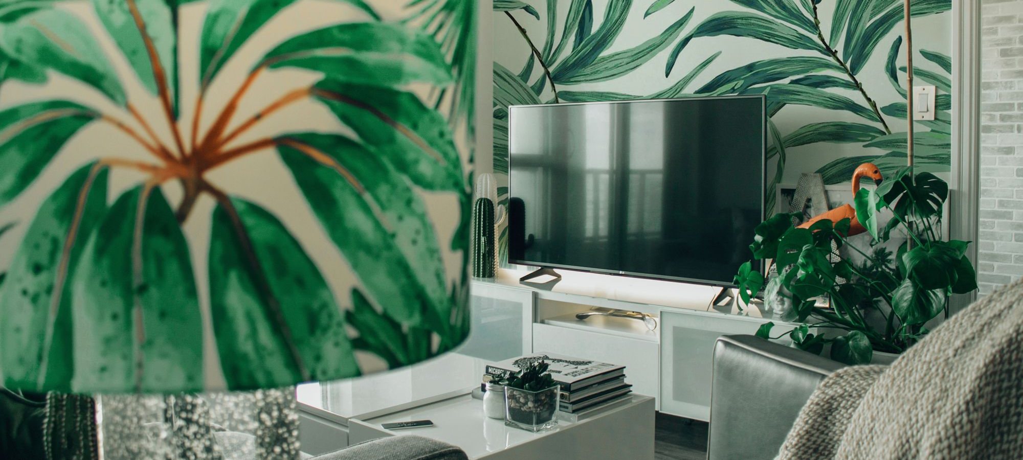 Living room with a tropical green palm-leaf mural wallpaper behind a media console